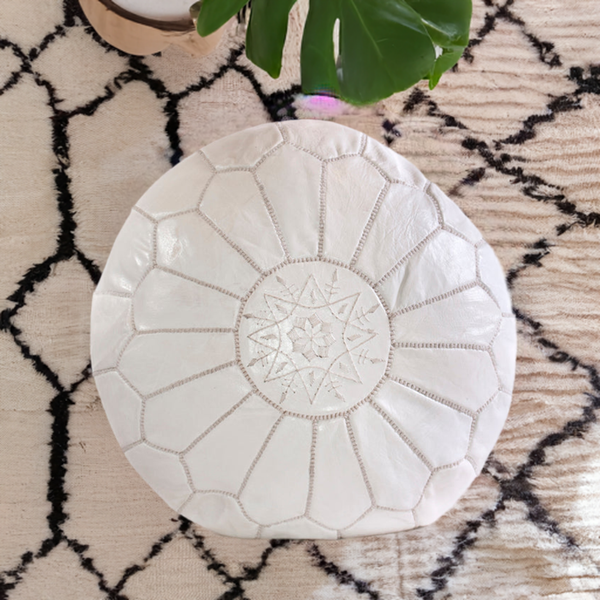 White Moroccan leather ottoman pouffe on patterned rug, hand-stitched detail, artisan-made.